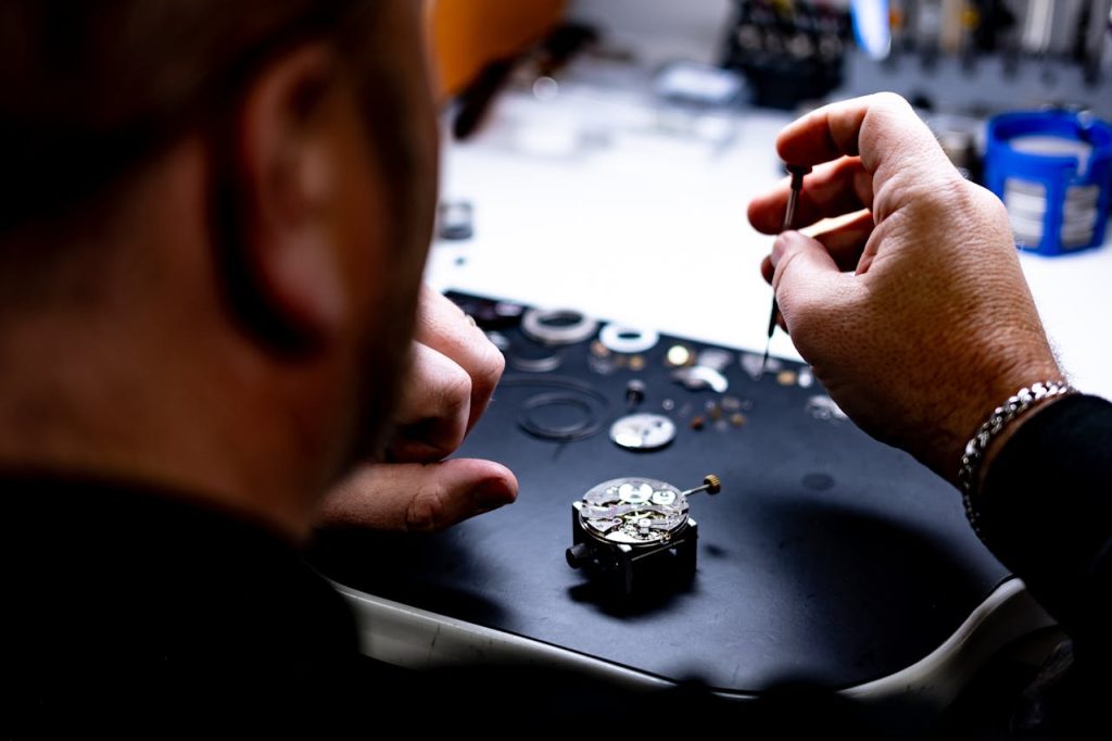 A skilled watch repair technician working on complex timepiece assembly in a workshop.